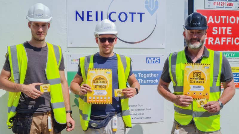 Three construction workers holding posters for new skin cancer campaign